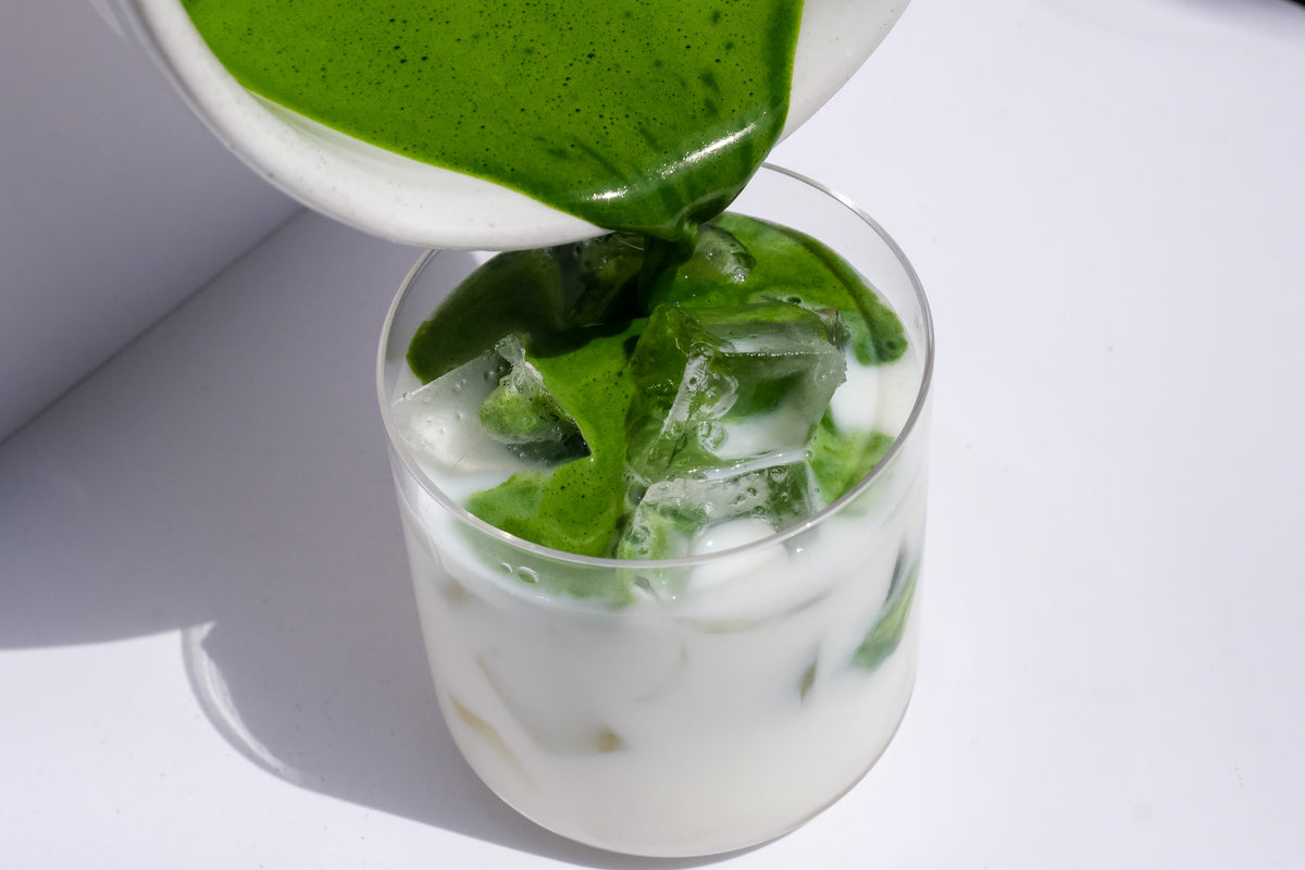 Yame Matcha being poured into a glass with ice cubes on a white background